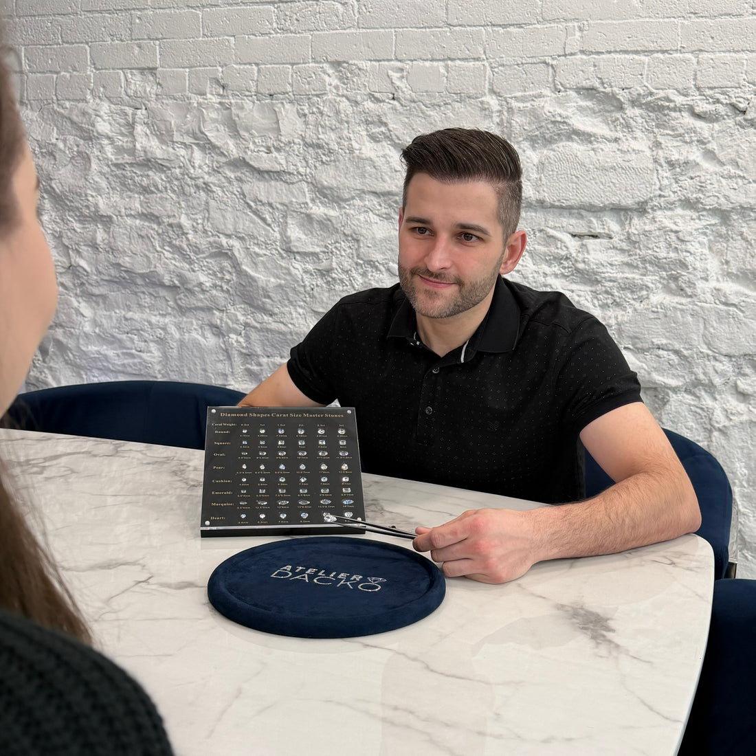Patrick from Atelier Dacko showing diamond shapes and carat size options at an in-office consultation for a custom engagement ring.