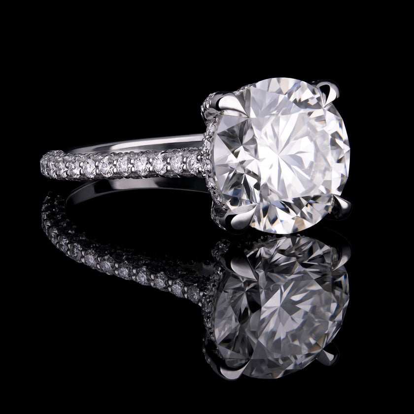 Engagement ring with large round brilliant-cut center stone in a prong setting, with a pavé band