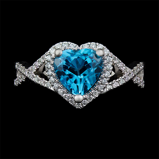 1.5 CT heart shaped topaz center stone set in 3 round prongs. Surrounded by diamonds in u-setting on the halo as well as diamonds on the ribbon style shank. Mount made in 14k white gold.