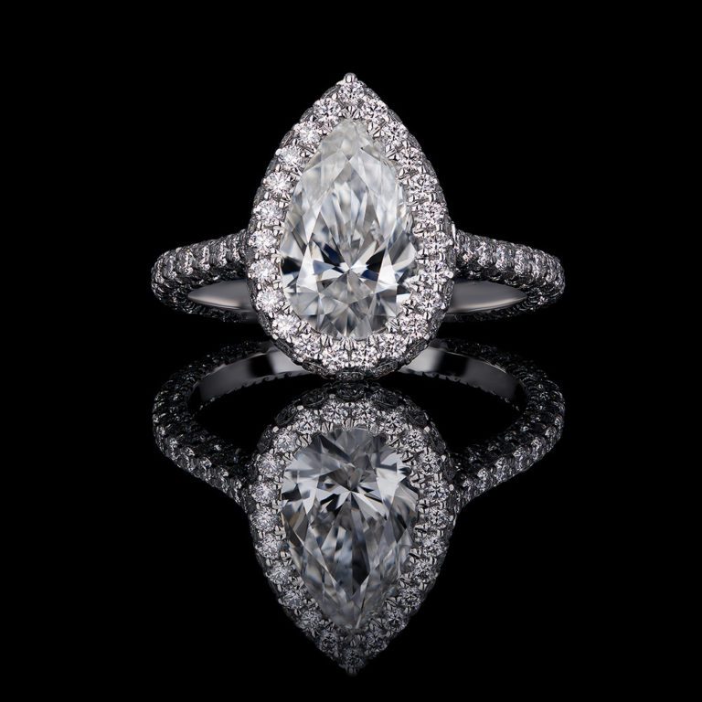 1.2 CT Pear shaped diamond center stone set in clawless halo with round diamonds. Featuring a second row of diamonds on the side of the halo, with a 3 sided pave shank on a platinum mount.