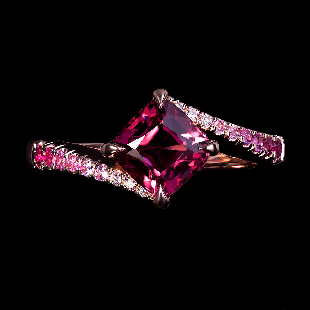 1.3 CT Cushion cut raspberry spinel center stone set in 14k rose gold mount with 4 talon claws. Accented by a gradation of pink sapphires u-set on the shank.