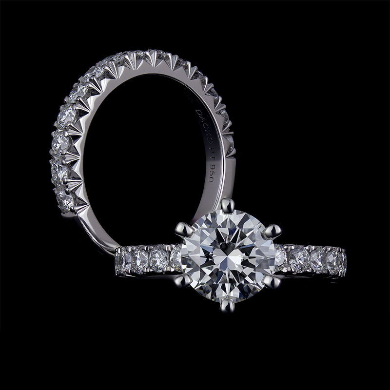 2 CT Round brilliant cut diamond set in platinum mount in 6 round prongs. The shank of the engagement ring is set in fishtail pave, with a matching fishtail pave cut wedding band in the background.