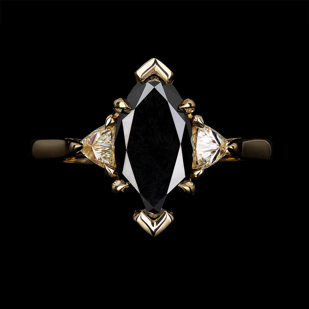 2 CT Marquise cut black diamond center with trillion cut white diamonds on the shoulders. The center stone is set in v-tip prongs on the tips and talon claws on the center. The trillion diamonds are set in 3 talon claws. The mount is in 14k yellow gold.